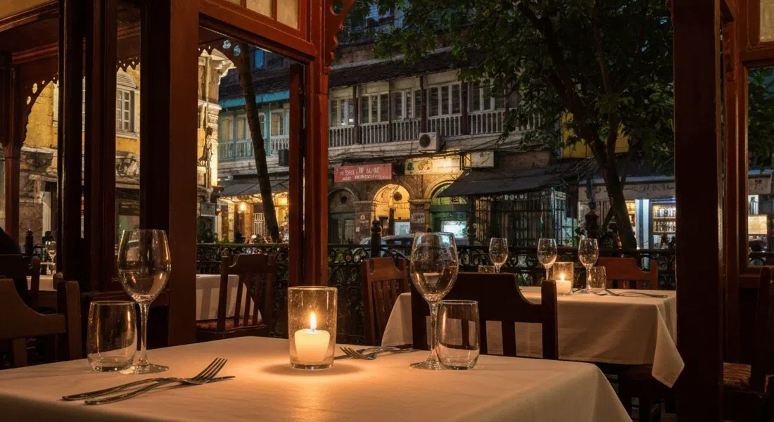 una mesa iluminada con velas dentro de Pali Village Cafe en Pali Mala Road, paredes de bungaló patrimonial y copas de vino brillando suavemente