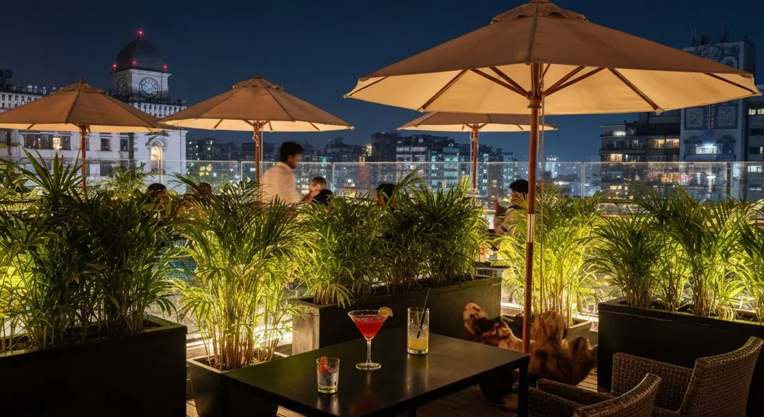 terraza de la azotea de Bonobo en Linking Road de noche, vegetación densa, sombrillas en forma de hongo y copas de cóctel con luz tenue